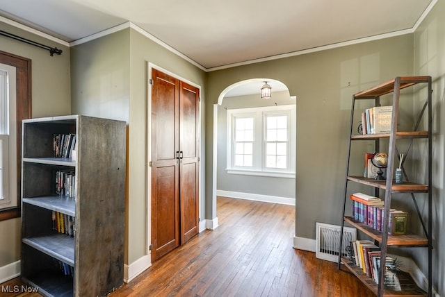 hallway featuring hardwood / wood-style floors, baseboards, arched walkways, and ornamental molding