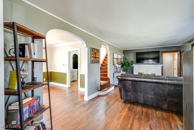 living area featuring wood finished floors, a fireplace, crown molding, baseboards, and stairs