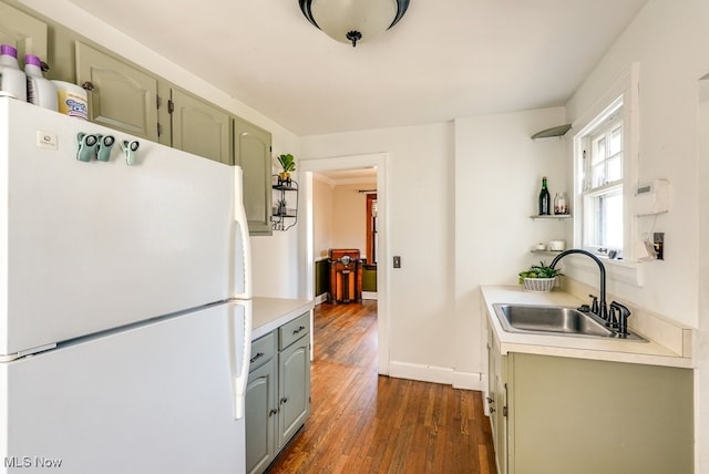 kitchen with a sink, baseboards, light countertops, freestanding refrigerator, and dark wood-style flooring