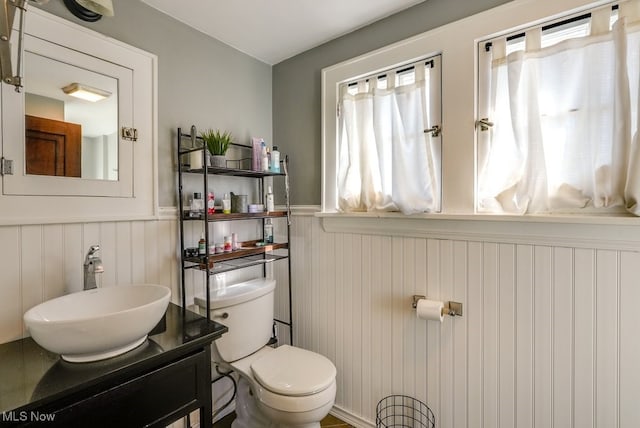 bathroom with vanity, toilet, and a wainscoted wall