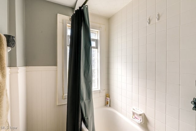 full bathroom with a wealth of natural light, a wainscoted wall, and shower / bathtub combination with curtain