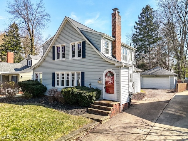 view of front of home with entry steps, a chimney, a detached garage, and an outdoor structure