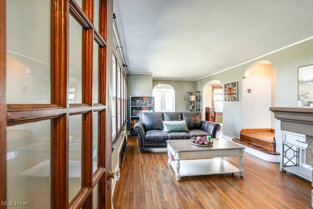 living room with arched walkways, dark wood-style floors, and crown molding