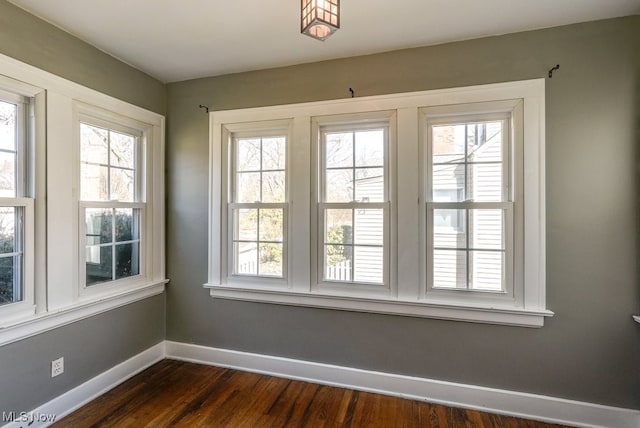 unfurnished room featuring a wealth of natural light, baseboards, and dark wood-type flooring