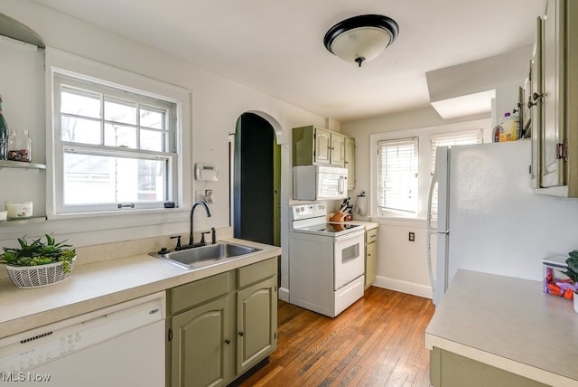 kitchen featuring white appliances, green cabinetry, light wood-style flooring, a sink, and light countertops