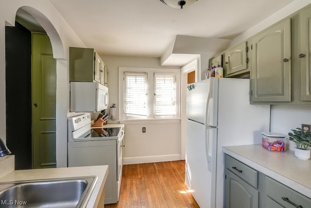 kitchen with light countertops, light wood-style flooring, washer / dryer, arched walkways, and white appliances