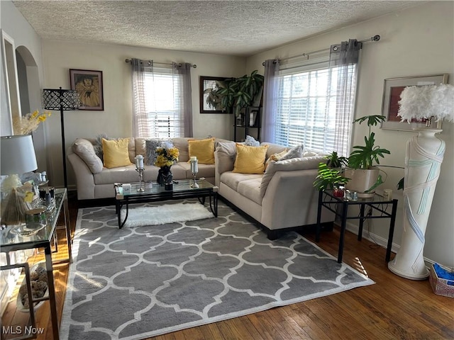 living area featuring a wealth of natural light, arched walkways, wood-type flooring, and a textured ceiling