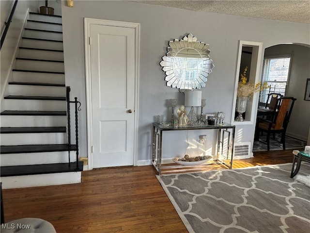 interior space with visible vents, baseboards, wood finished floors, arched walkways, and a textured ceiling