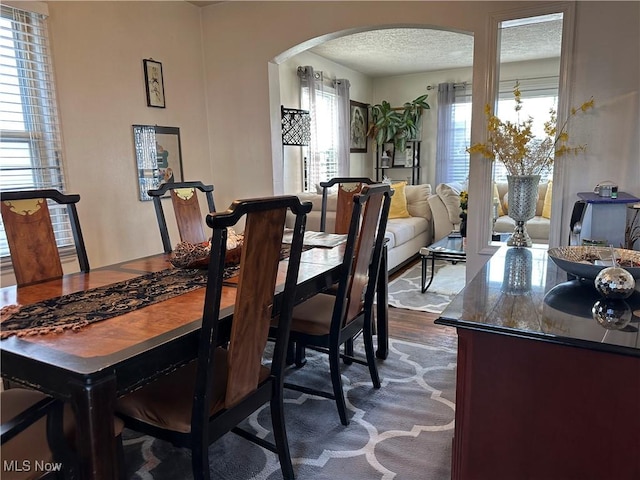 dining space featuring arched walkways, dark wood-style floors, and a textured ceiling