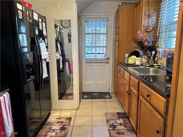 kitchen featuring a sink, black fridge with ice dispenser, dark countertops, brown cabinetry, and light tile patterned floors