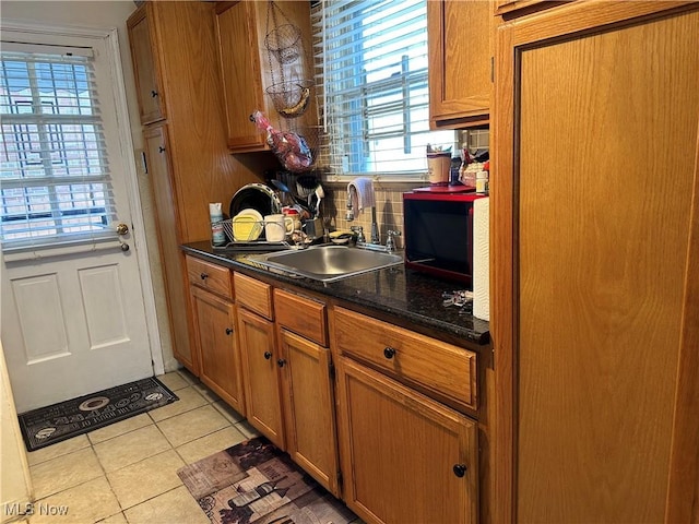 kitchen featuring dark countertops, backsplash, brown cabinetry, light tile patterned flooring, and a sink