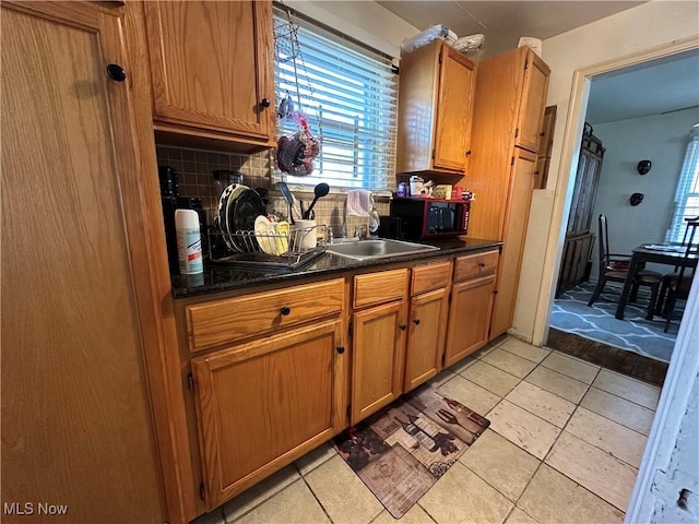 kitchen with dark countertops, backsplash, black microwave, light tile patterned floors, and a sink