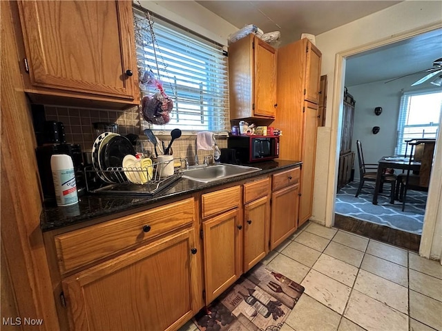 kitchen featuring tasteful backsplash, dark countertops, black microwave, brown cabinets, and a sink