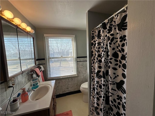 bathroom with a wainscoted wall, toilet, a shower with shower curtain, tile walls, and vanity