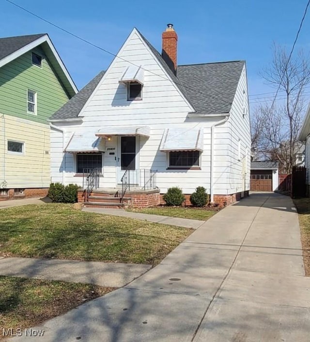 view of front facade featuring a front yard, an outbuilding, roof with shingles, and a chimney