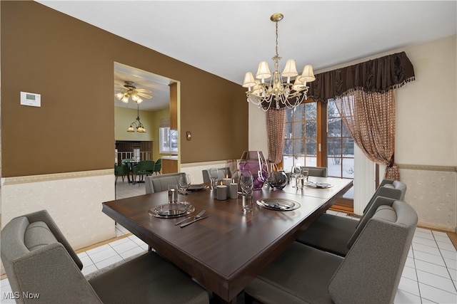 dining room with light tile patterned floors, ceiling fan with notable chandelier, wainscoting, and wallpapered walls