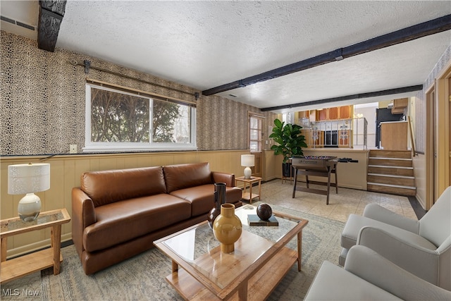 living room with visible vents, a wainscoted wall, stairs, a textured ceiling, and beamed ceiling