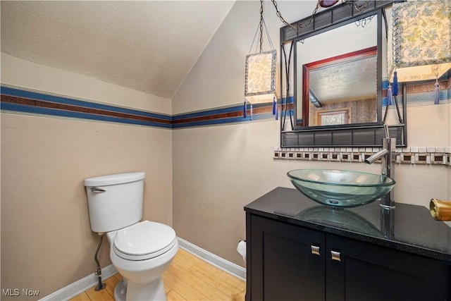 half bathroom featuring toilet, a textured ceiling, baseboards, vanity, and vaulted ceiling