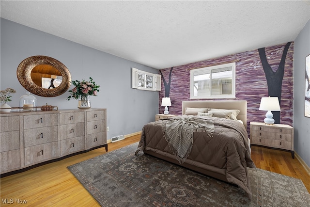 bedroom with visible vents, baseboards, a textured ceiling, and wood finished floors