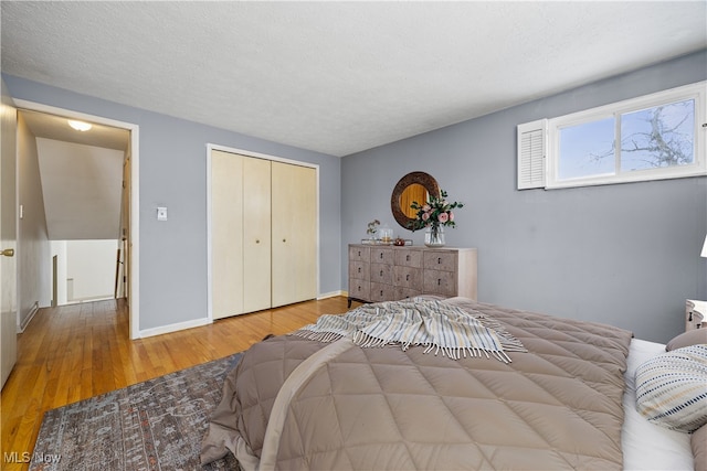 bedroom with a closet, baseboards, a textured ceiling, and wood finished floors