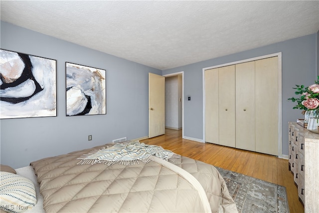 bedroom with visible vents, baseboards, light wood-style floors, a closet, and a textured ceiling