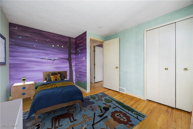 bedroom featuring visible vents, a textured ceiling, wood finished floors, a closet, and baseboards