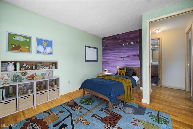 bedroom with an accent wall, wood finished floors, baseboards, and a textured ceiling