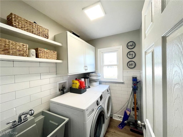 laundry area featuring dark wood-style floors, washing machine and clothes dryer, cabinet space, a sink, and tile walls