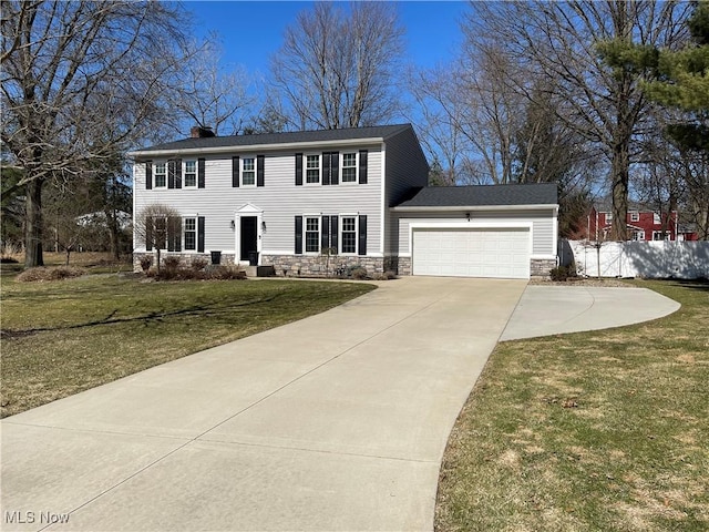 colonial house with stone siding, an attached garage, a front lawn, and fence