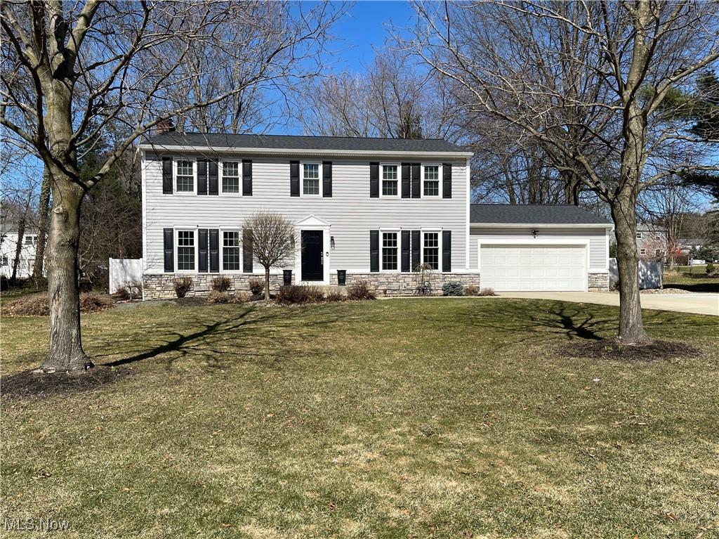 colonial home with a front lawn, stone siding, concrete driveway, a garage, and a chimney