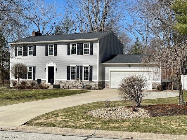 colonial-style house featuring a front yard, a chimney, driveway, stone siding, and an attached garage