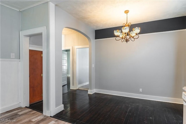 unfurnished dining area with arched walkways, a chandelier, dark wood-type flooring, and baseboards