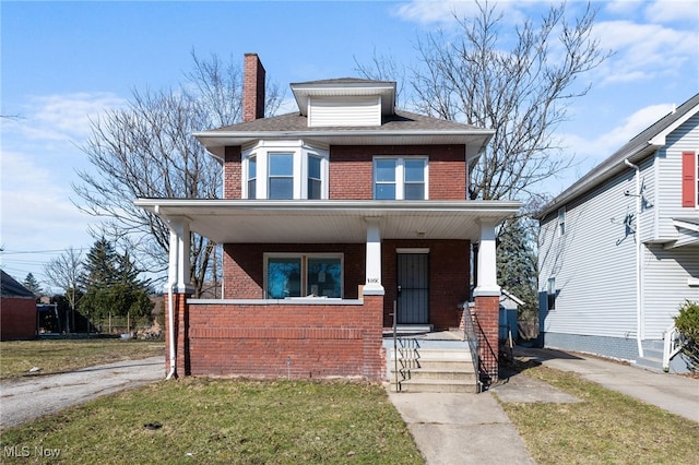 american foursquare style home featuring a chimney, brick siding, covered porch, and a front lawn