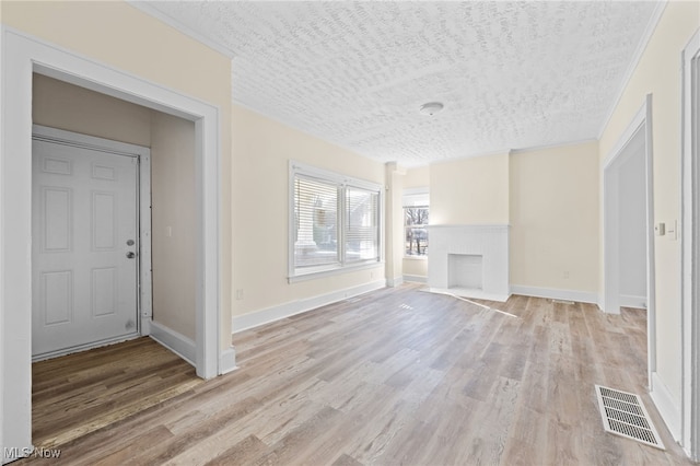 unfurnished living room with baseboards, visible vents, light wood finished floors, a fireplace, and a textured ceiling