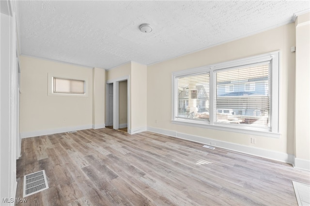 unfurnished room with light wood-type flooring, visible vents, baseboards, and a textured ceiling