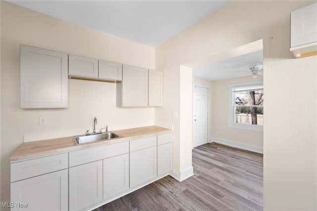 kitchen featuring wooden counters, a sink, wood finished floors, baseboards, and ceiling fan