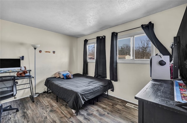 bedroom with visible vents, a textured ceiling, and wood finished floors