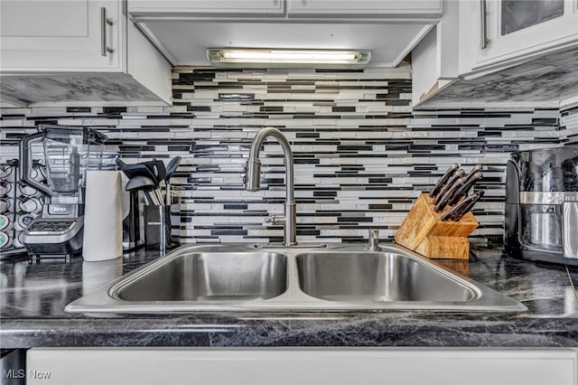 room details featuring a sink, tasteful backsplash, dark countertops, white cabinets, and glass insert cabinets