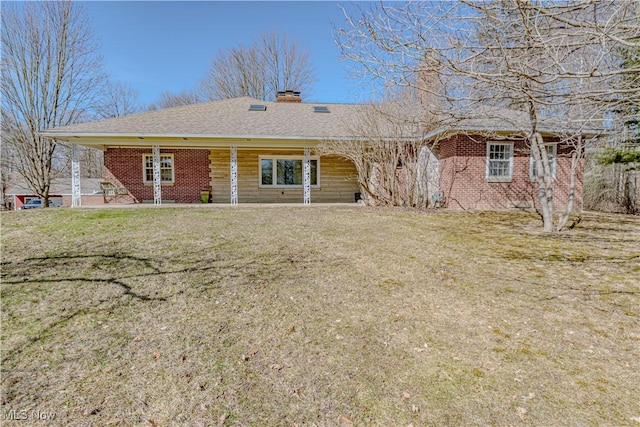 back of house with a lawn, brick siding, roof with shingles, and a chimney