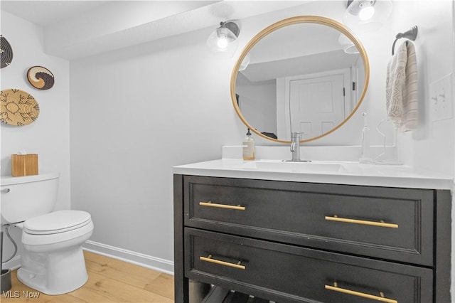 half bathroom featuring toilet, vanity, baseboards, and wood finished floors