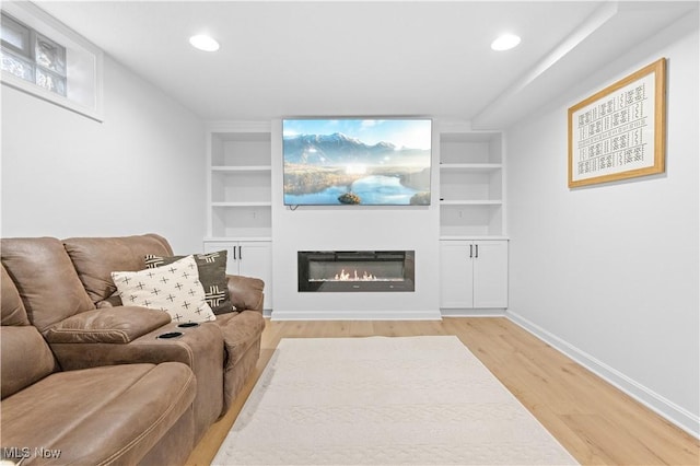 living room featuring a glass covered fireplace, built in shelves, and light wood-type flooring