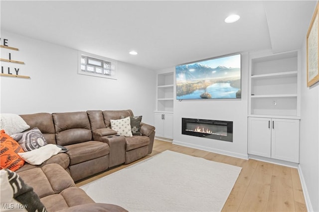 living room with a glass covered fireplace, built in features, light wood-style flooring, and recessed lighting