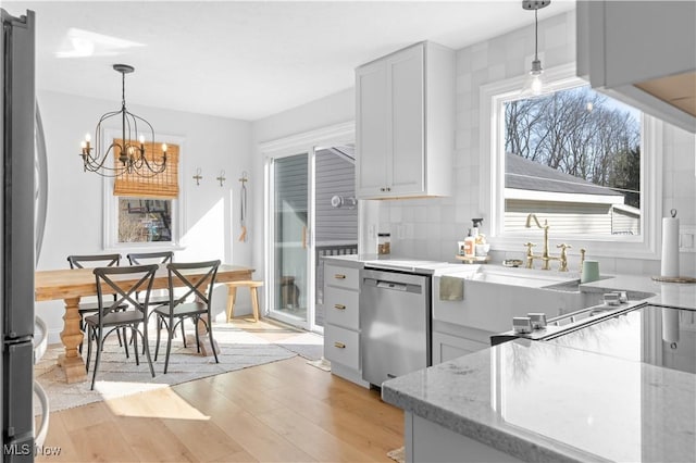 kitchen with light stone countertops, light wood-style flooring, stainless steel appliances, hanging light fixtures, and tasteful backsplash