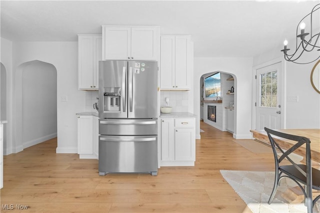 kitchen with white cabinetry, arched walkways, stainless steel fridge, and backsplash