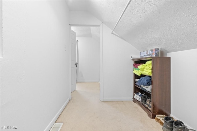 hallway with visible vents, a textured ceiling, baseboards, carpet flooring, and lofted ceiling