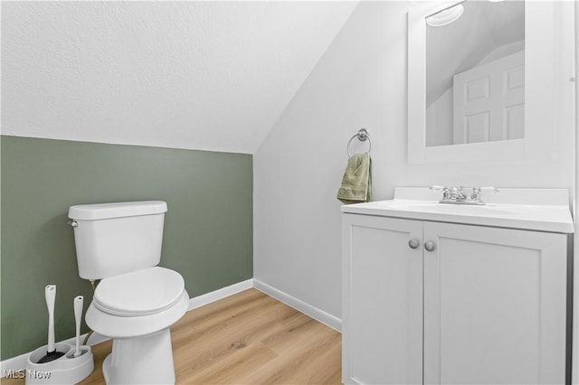 half bathroom with baseboards, toilet, vaulted ceiling, wood finished floors, and vanity