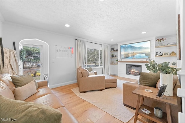 living room featuring light wood-style flooring, a textured ceiling, a glass covered fireplace, recessed lighting, and baseboards