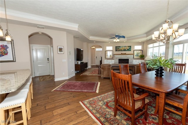 dining area with hardwood / wood-style flooring, arched walkways, crown molding, a fireplace, and a raised ceiling