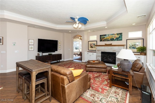 living room with a high end fireplace, wood finished floors, a tray ceiling, and ornamental molding