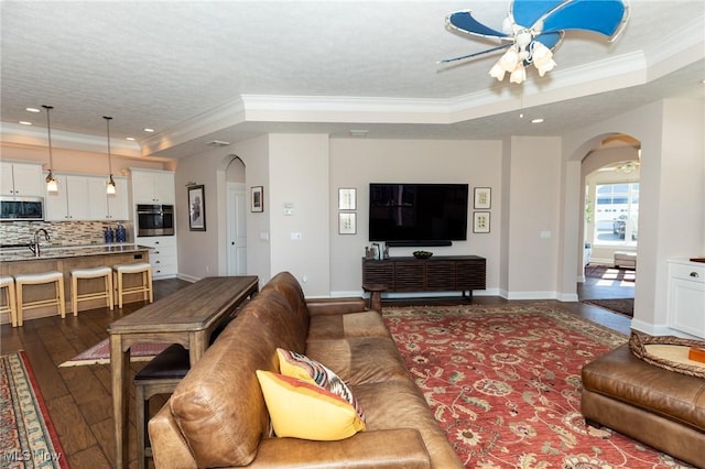 living area featuring a raised ceiling, arched walkways, dark wood-style flooring, and ornamental molding